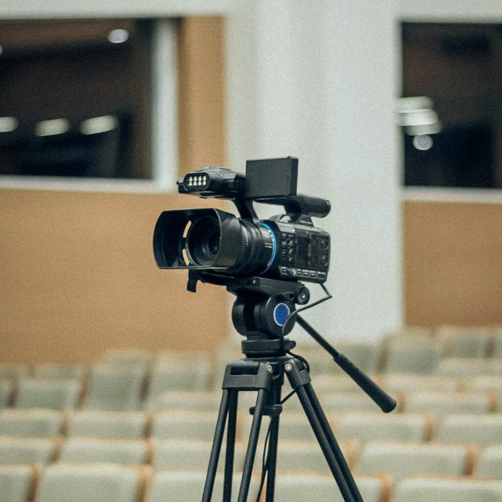 Close-up of a video camera set up on a tripod in an empty auditorium.